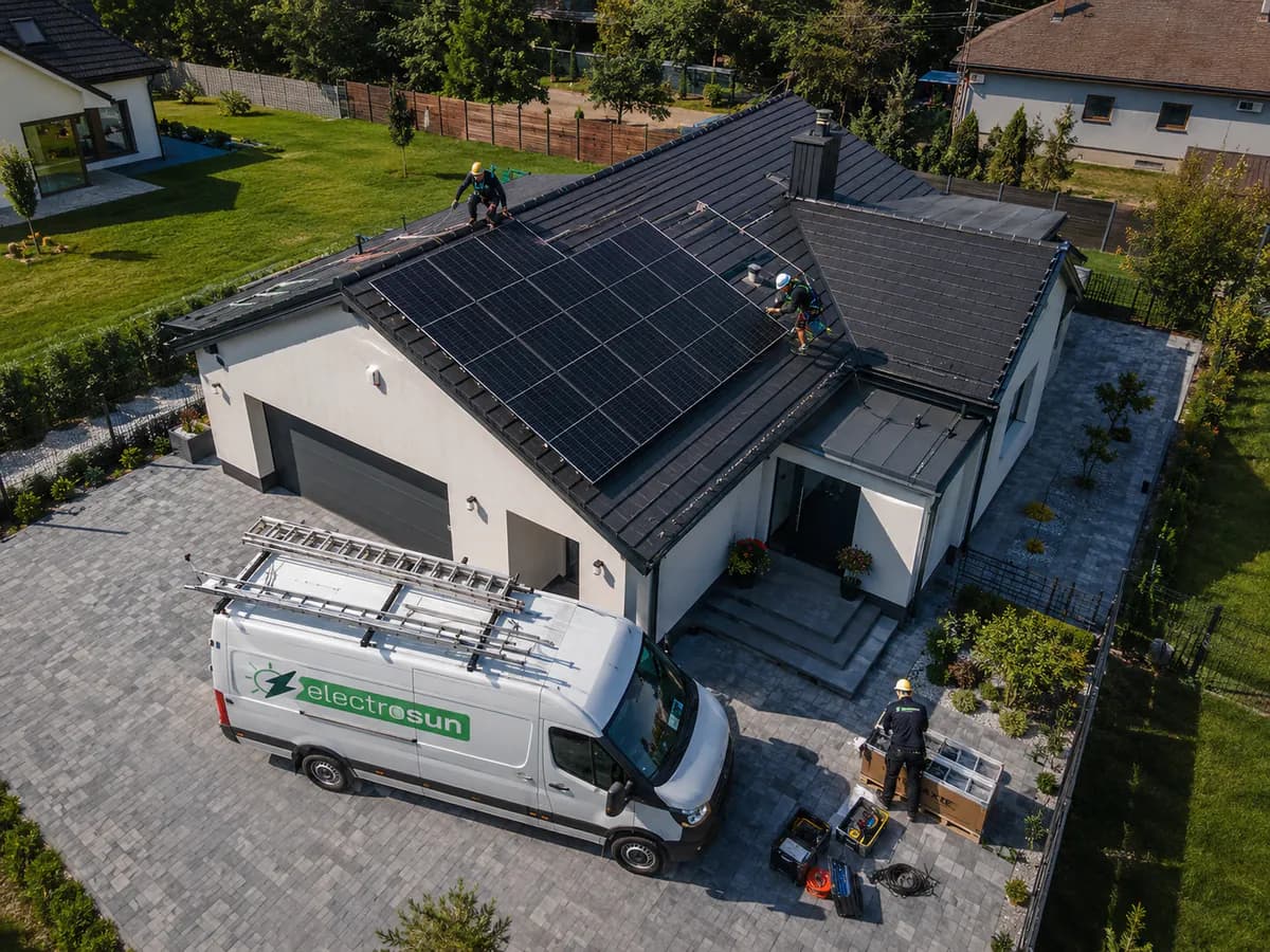 Echipa ElectroSun montând panouri fotovoltaice pe acoperișul unei case, cu duba de serviciu parcată în curte